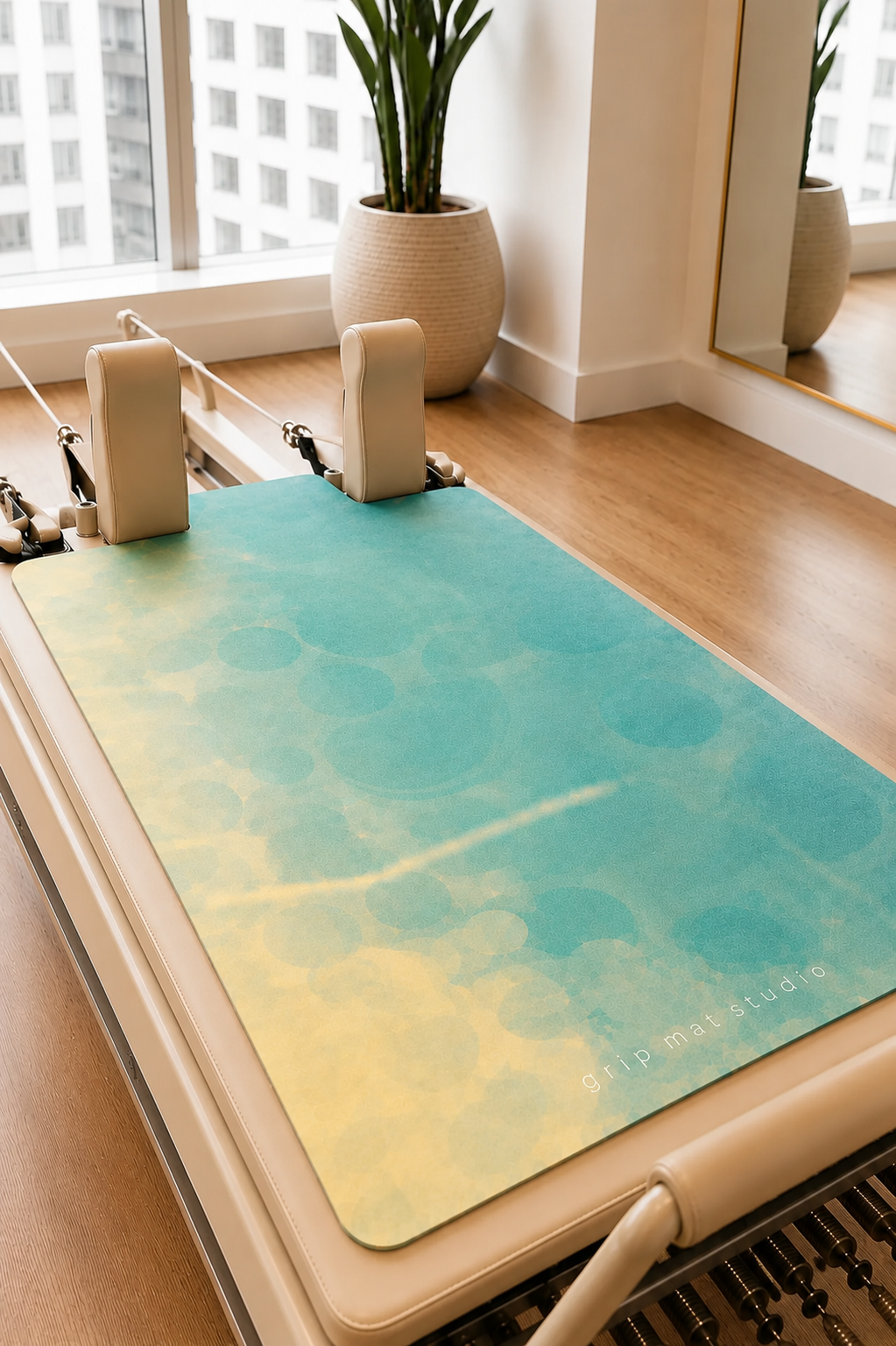 Sunlit Waters aqua and gold Pilates reformer grip mat displayed on a beige commercial studio reformer.