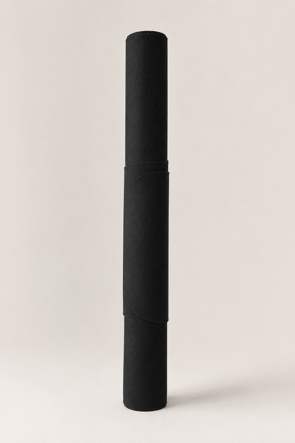 A black rolled-up yoga mat standing vertically on a clean, light beige studio background.