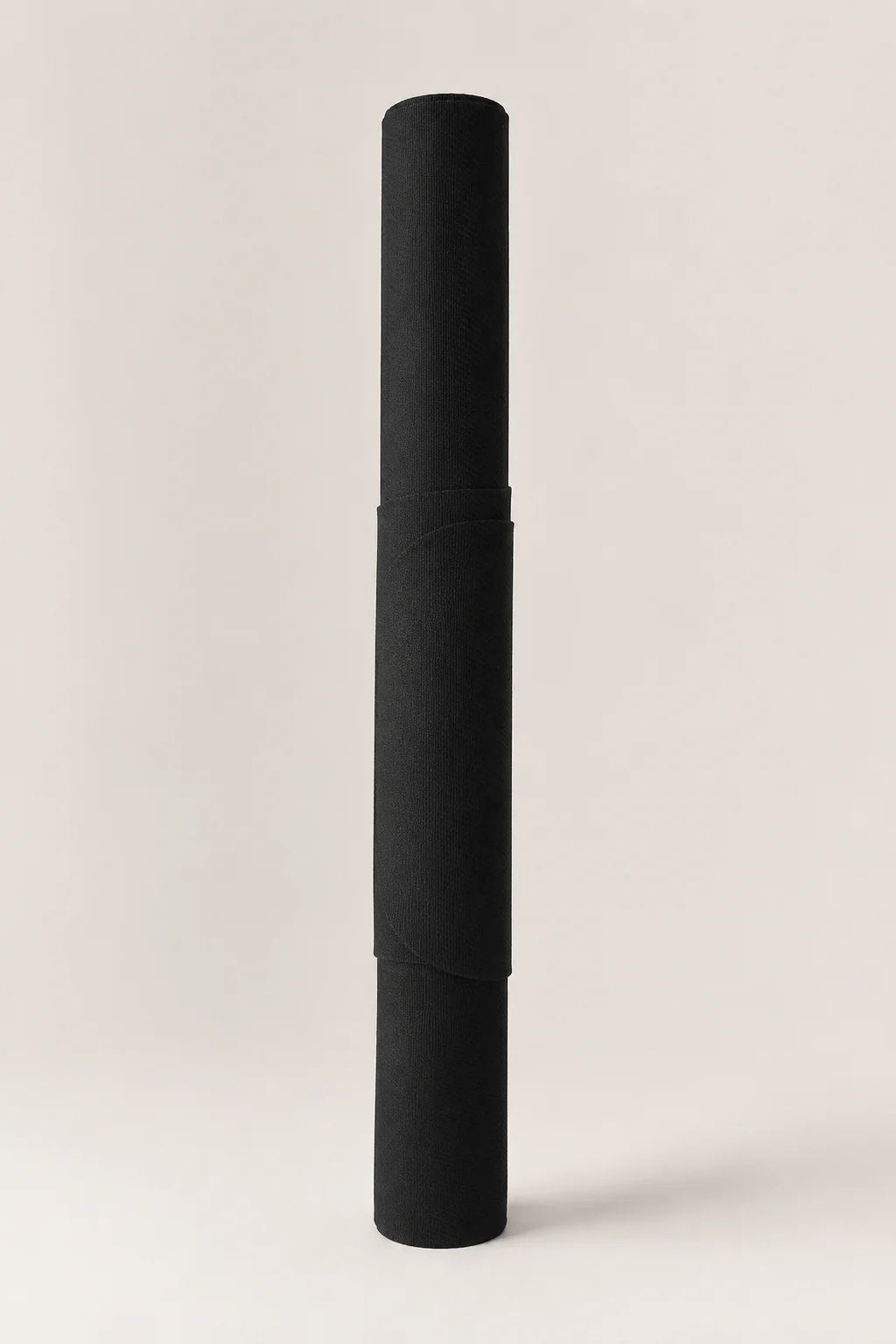 A black rolled-up fabric item, likely a towel or blanket, standing vertically on a light beige background.