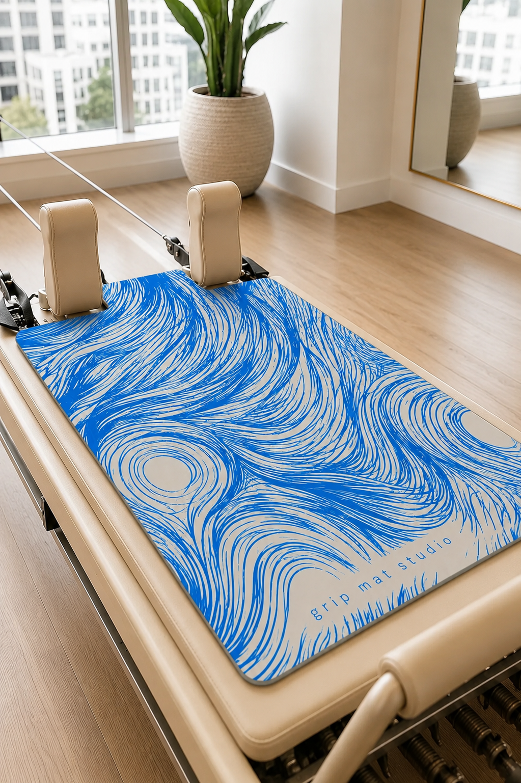 A commercial studio Pilates reformer machine in a bright studio, featuring a blue and white swirling patterned mat with the text 'rip mat studio' printed on it.