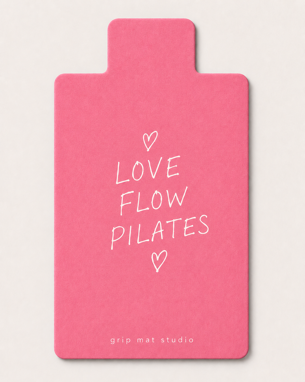 A pink grip mat with white text reading 'LOVE FLOW PILATES' and small heart illustrations, shown on a light neutral background. The brand name 'grip mat studio' is printed at the bottom.