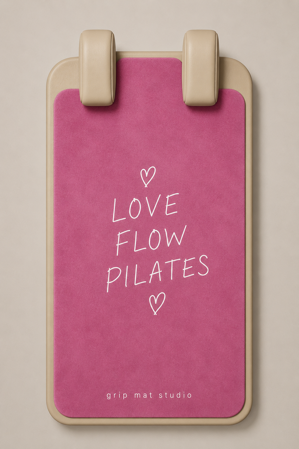 A pink grip mat with a beige border and two beige handle grips at the top, featuring the white text 'LOVE FLOW PILATES' and small heart illustrations on the front. The brand 'grip mat studio' is printed at the bottom.
